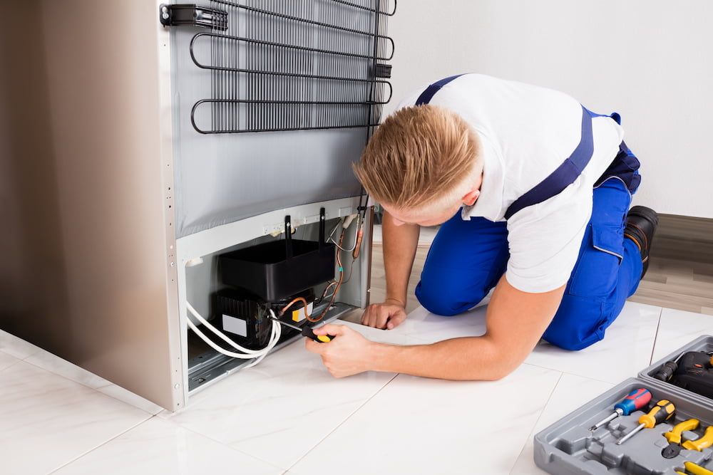 Ein Handwerker arbeitet an einem Kühlschrank und verwendet Werkzeuge zur Durchführung der Reparatur.